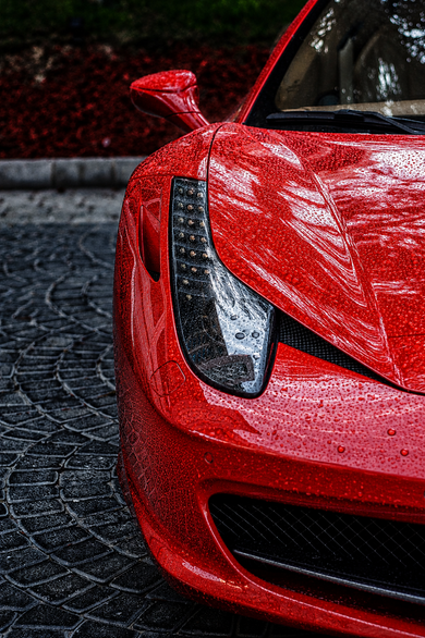Water beads forming on the protected red paint of a sports car, illustrating hydrophobic surface behaviour.