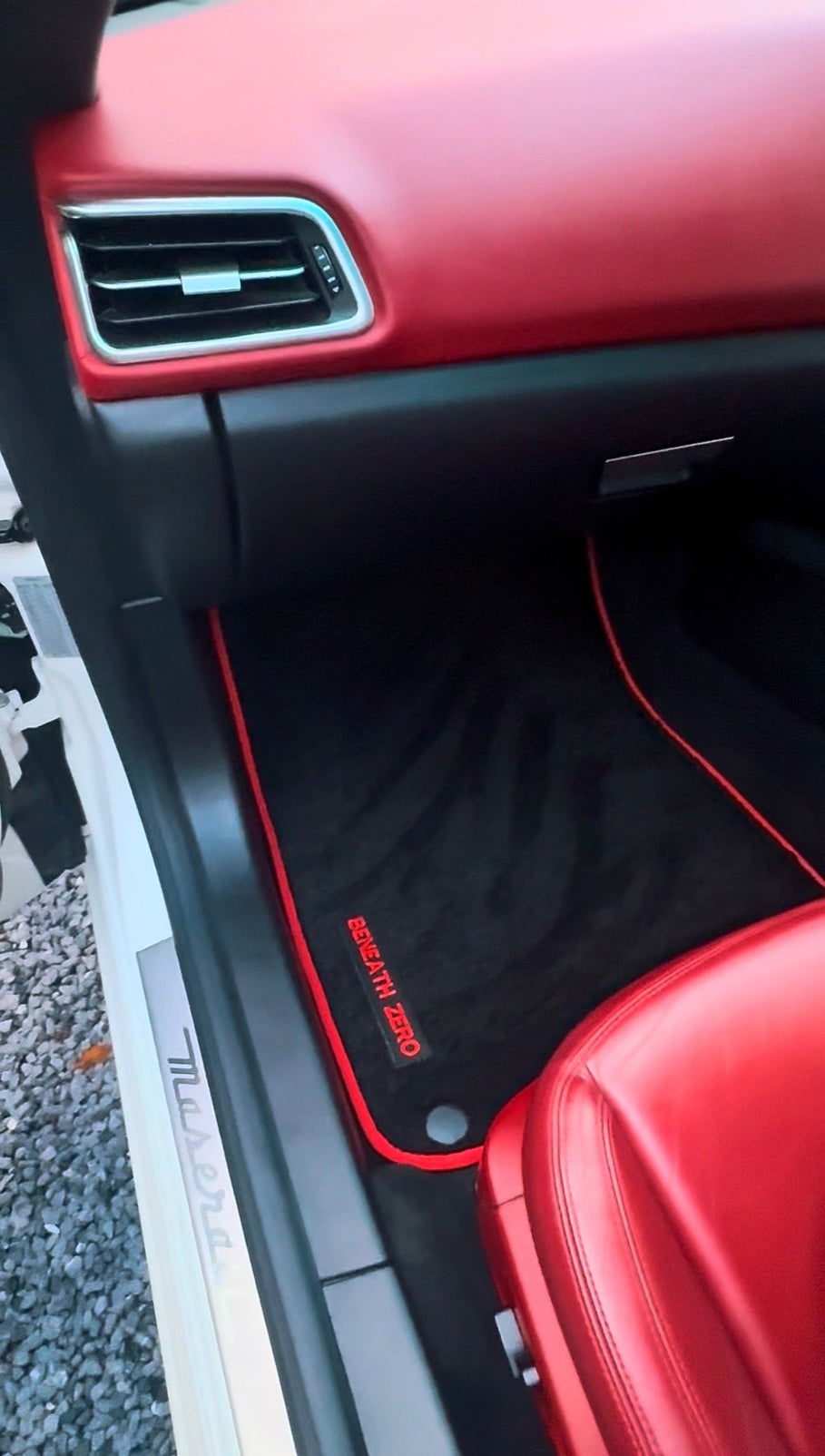 Car floor mat being vacuumed and cleaned inside an open boot used as a temporary raised detailing workstation.